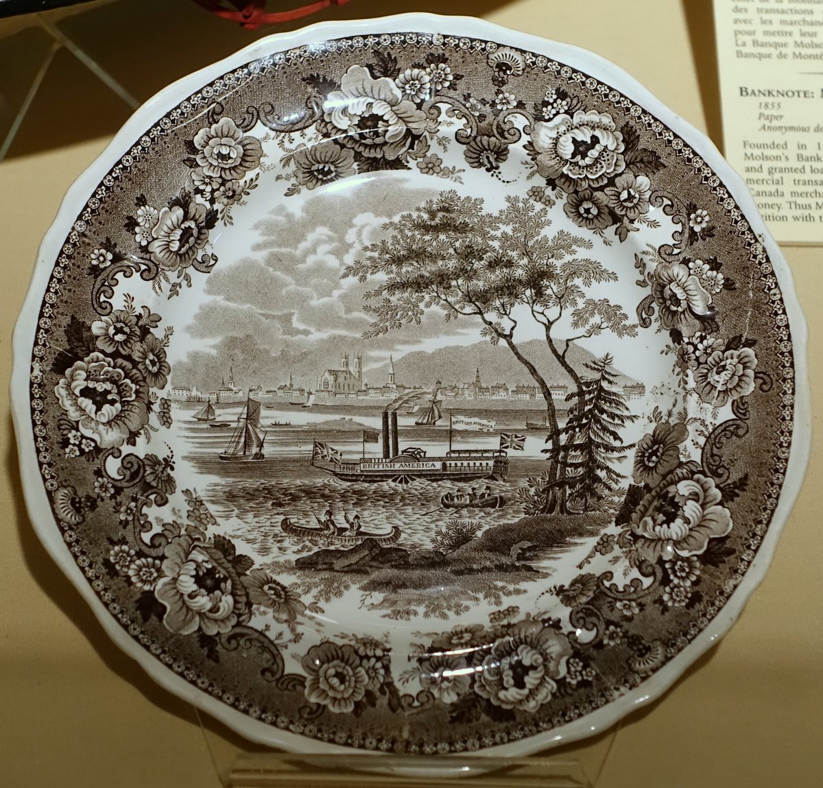 Brown-and-white plate with a floral border and a steamship marked British America in a waterfront scene