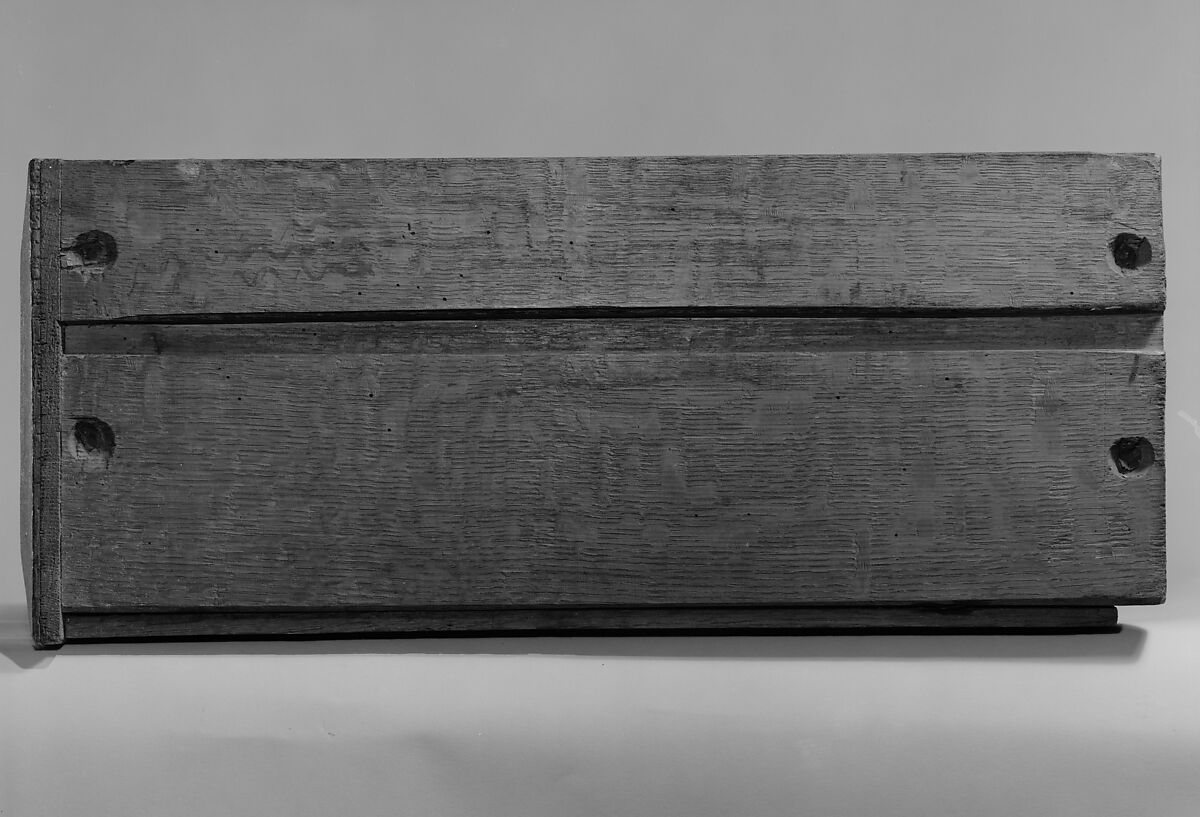 Black-and-white museum photograph of a wooden drawer underside, showing boards, grain and recessed fastenings